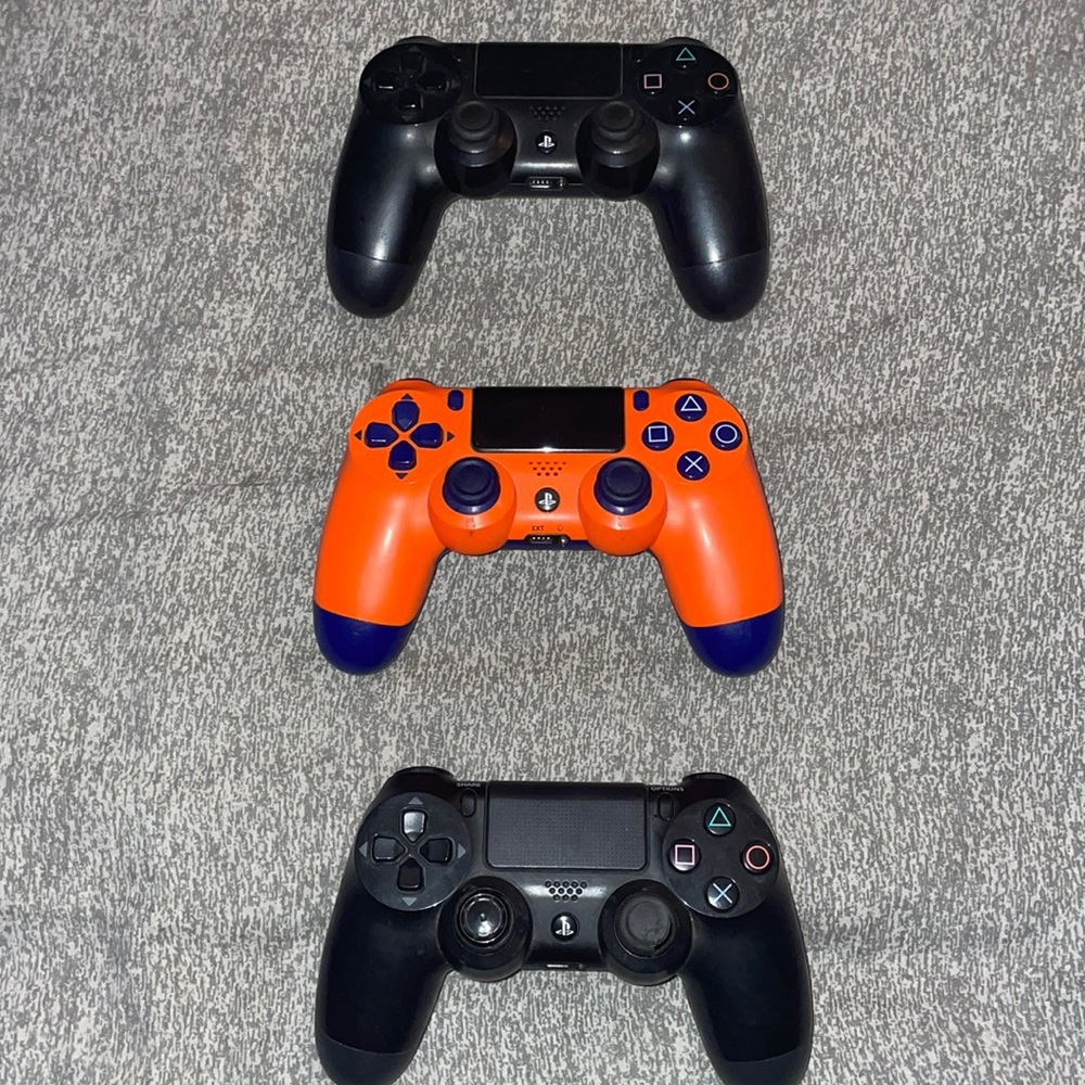 2 black PlayStation controllers and one Crash Bandicoot edition controller.
